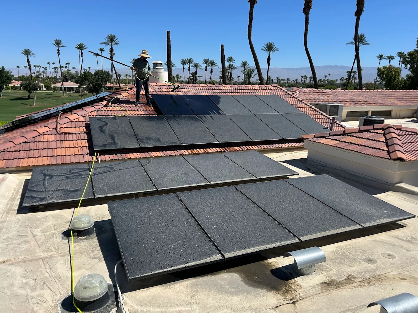 Glossy technician cleaning a large rooftop solar array in the Coachella Valley